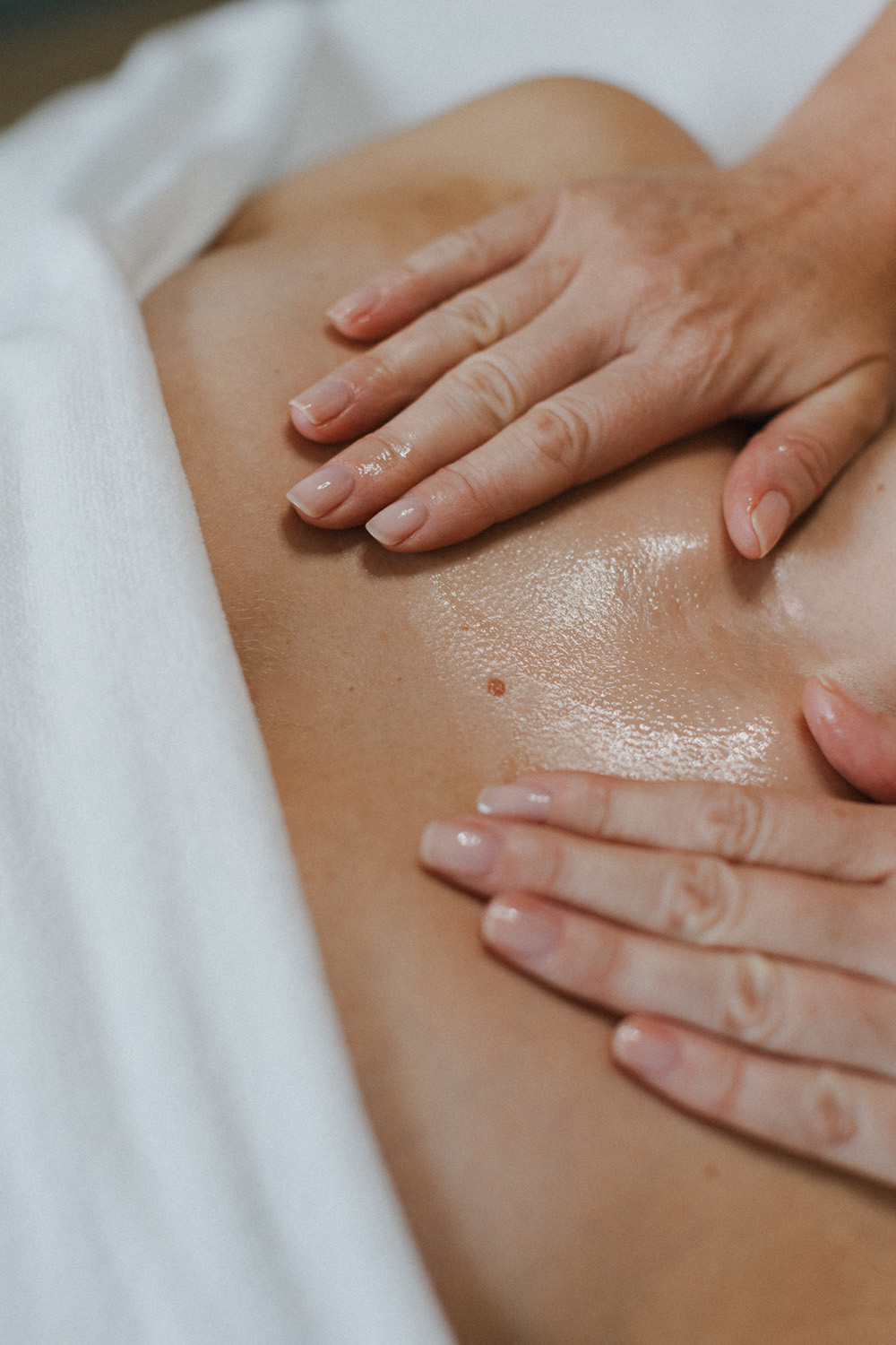 Nahaufnahme von Händen, die Öl auf den öligen Rücken einer Person während einer Massage auftragen.