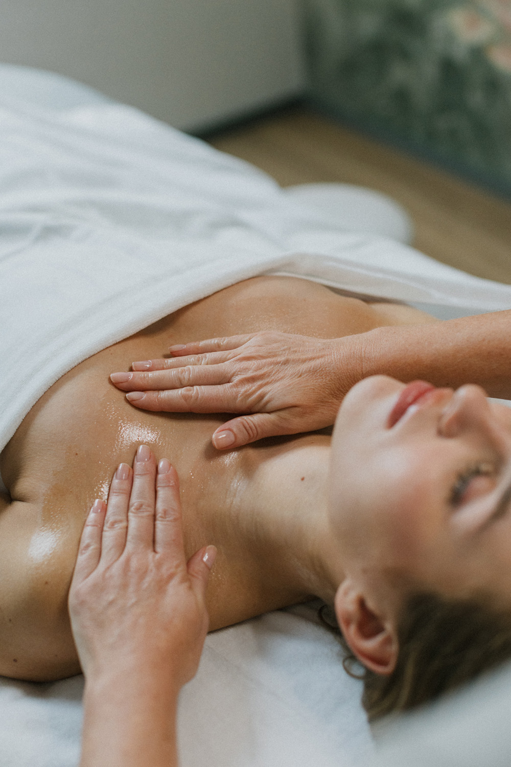 Frau liegt entspannt auf einer Massageliege und erhält eine Brust- und Schulter-Massage mit Öl.