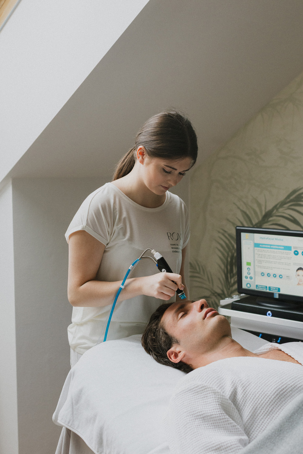 Kosmetikerin führt eine Gesichtsbehandlung mit einem elektrischen Gerät bei einem entspannten Mann durch.