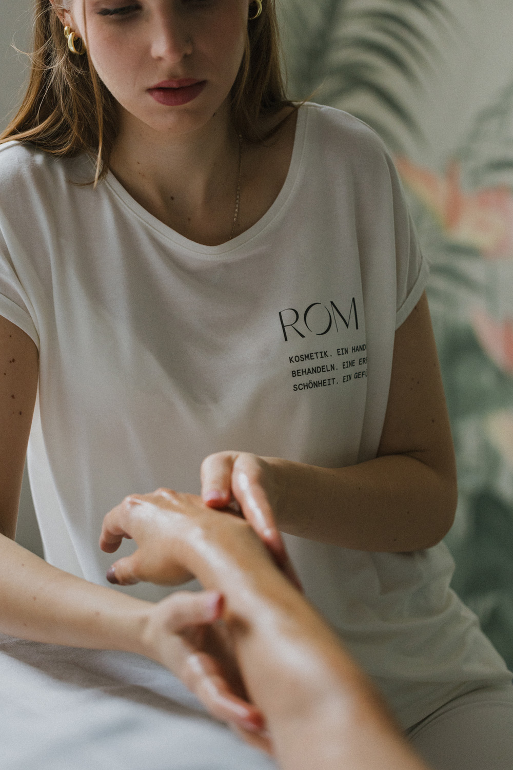 Frau in weißem T-Shirt massiert behutsam den Unterarm einer anderen Person.