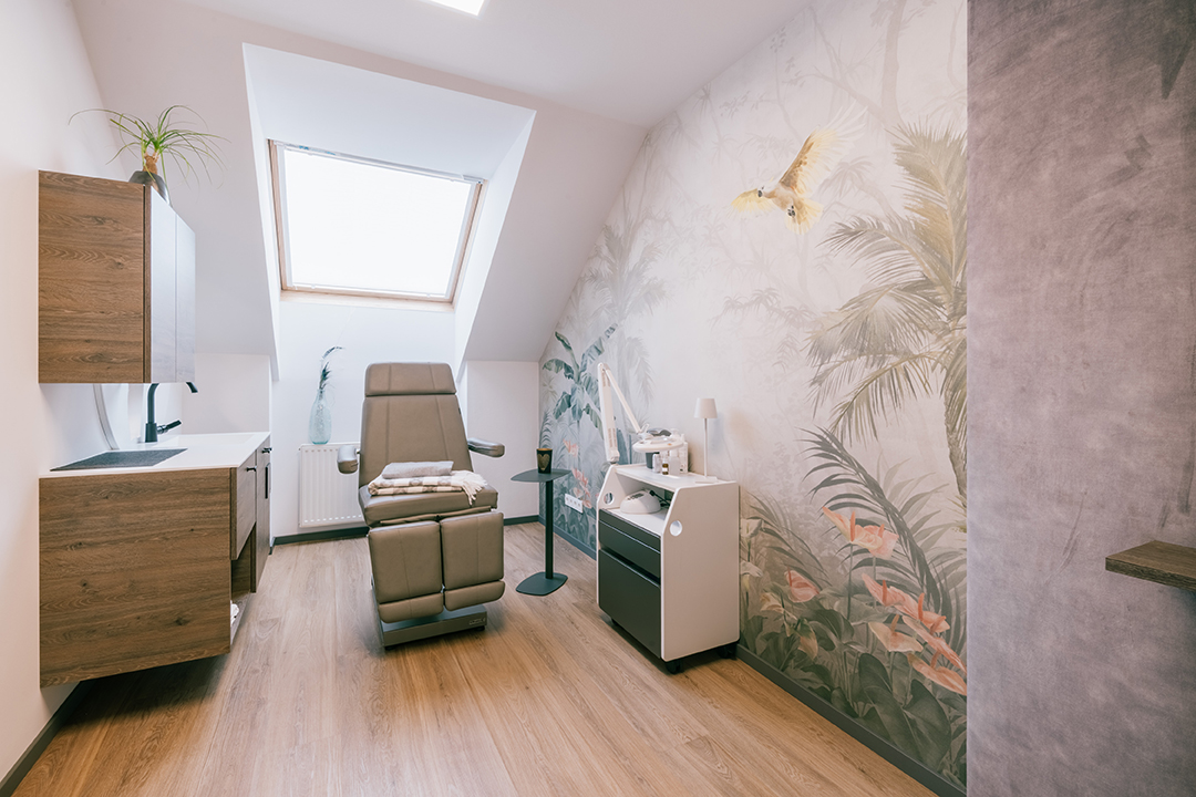 Moderne Praxis mit Behandlungsliege unter einem Dachfenster und einer Wand mit Dschungel-Wandbild.