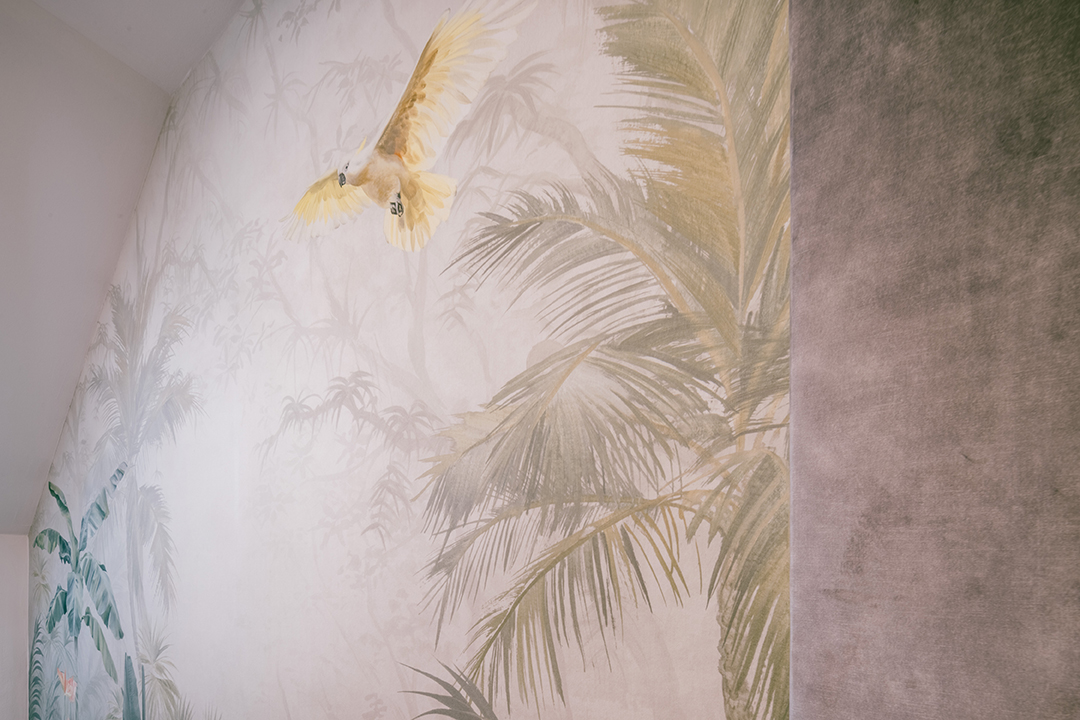 Wandgemälde mit einer fliegenden gelben Kakadu und tropischen grünen Palmenblättern.