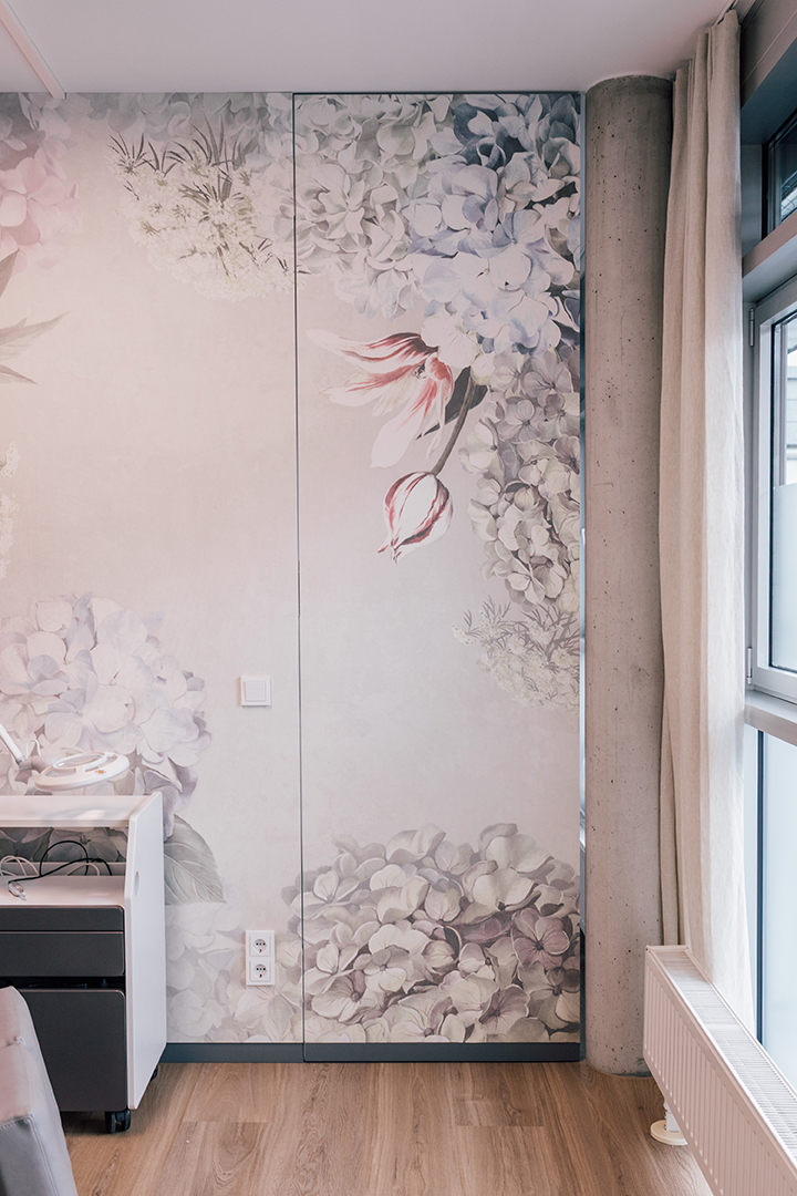 Wand mit großem blumigem Wandbild in sanften Pastellfarben neben Fenster mit Vorhang und Betonstütze in einem modernen Raum.