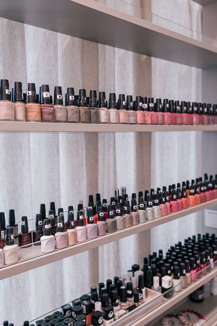 Reihen von Nagellackflaschen in verschiedenen Farben auf drei Regalböden in einem Kosmetikstudio.