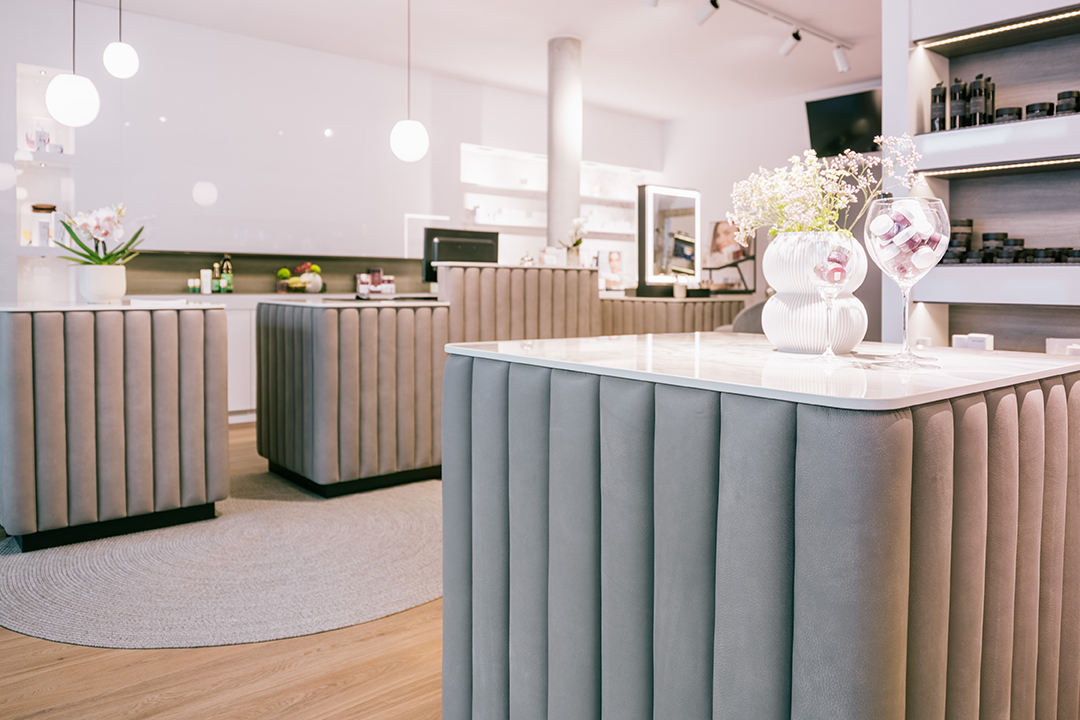 Modernes Geschäft mit samtbezogenen Theken, Blumentopf mit weißen Blumen und Weinglas mit Produkten.