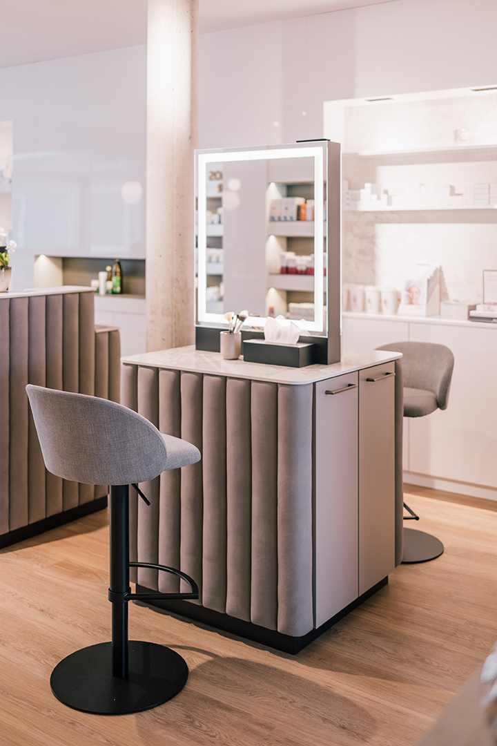 Moderner Schminktisch mit beleuchtetem Spiegel und grauem Barhocker in einem hellen, eleganten Raum.