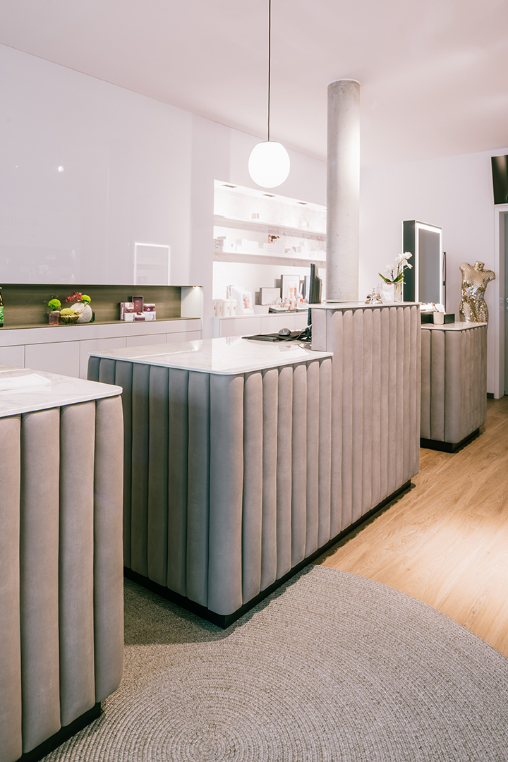 Modernes Empfangsbereich mit grauen, vertikal gepolsterten Tresen, hellem Holzfußboden und runder Teppichmatte.