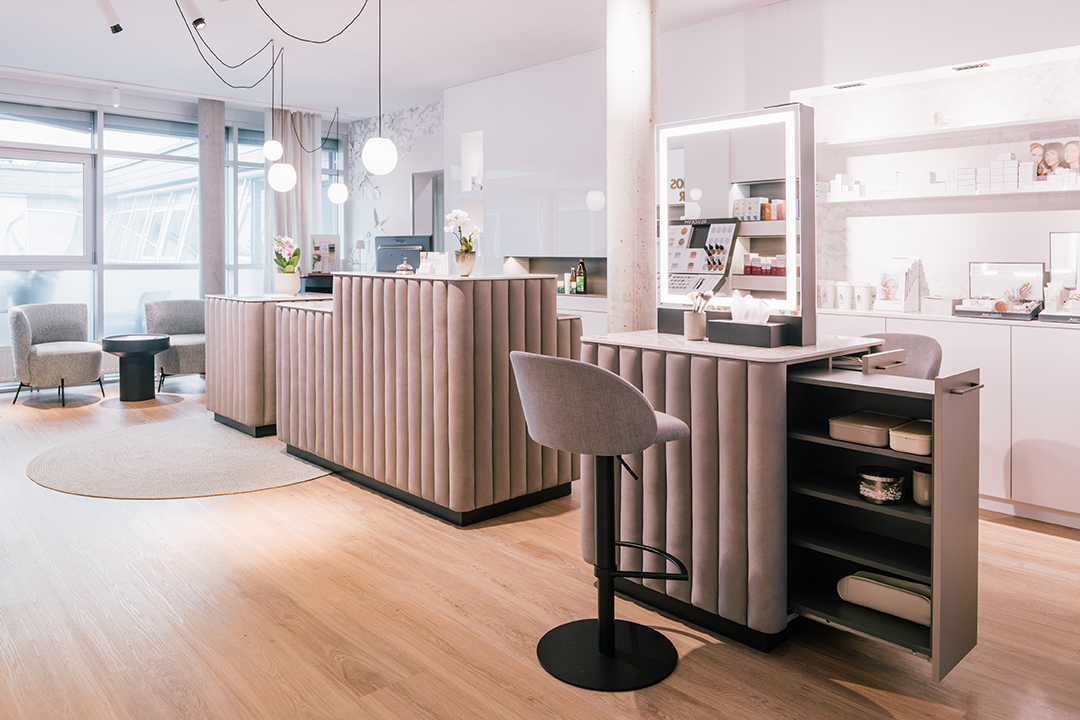 Heller, moderner Schönheits- oder Kosmetiksalon mit gepolsterten Empfangstheken, einem Spiegel mit Beleuchtung und gemütlichen Sitzgelegenheiten.