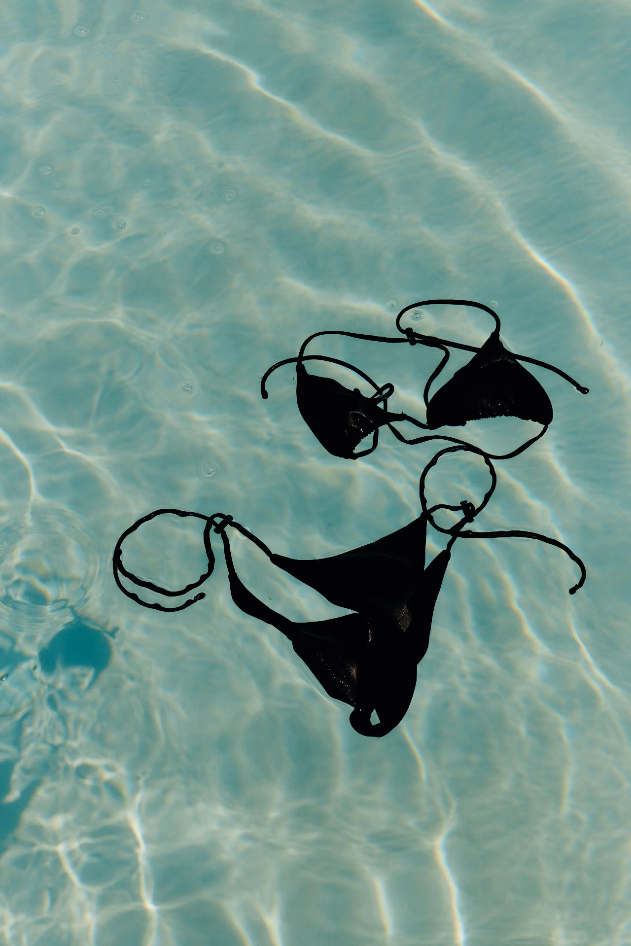 Schwarzer Bikini, der in klarem Wasser eines Schwimmbeckens schwimmt.
