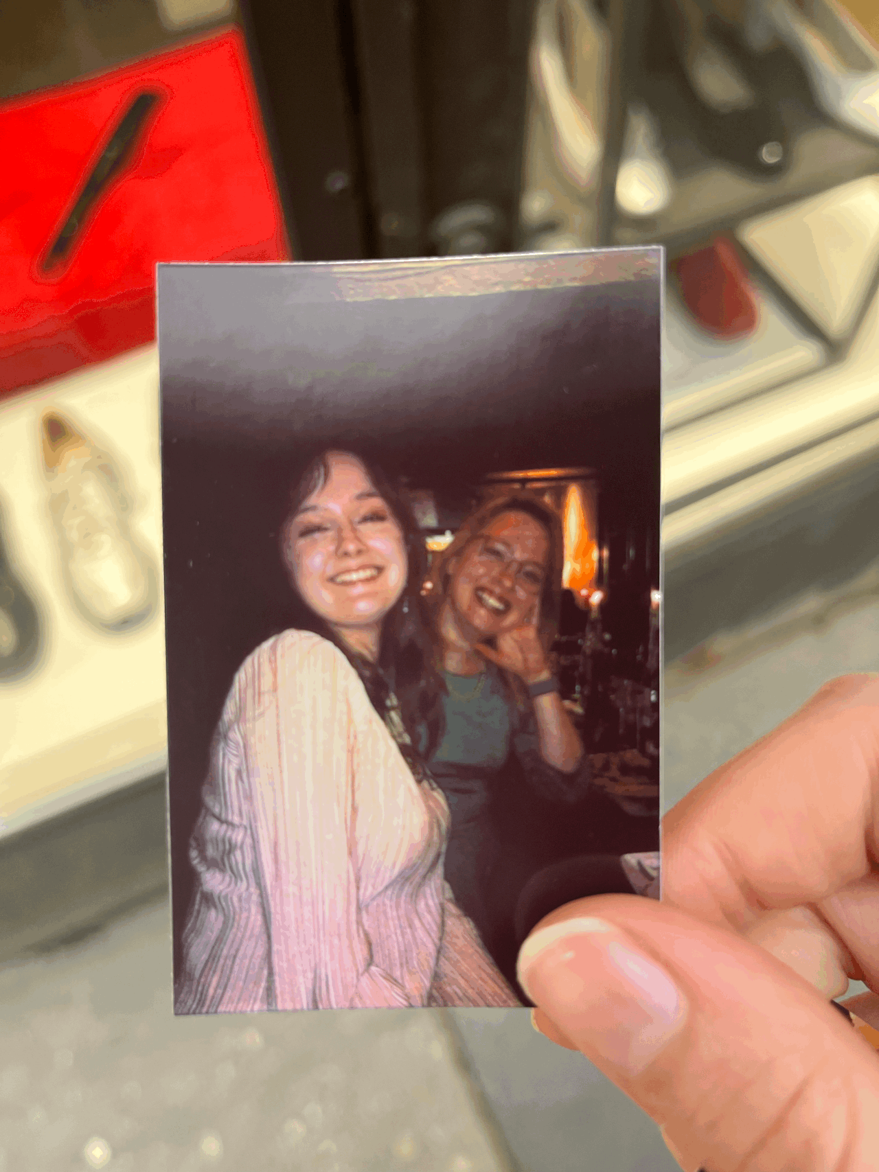Photo held by a hand showing two smiling women sitting closely together indoors.