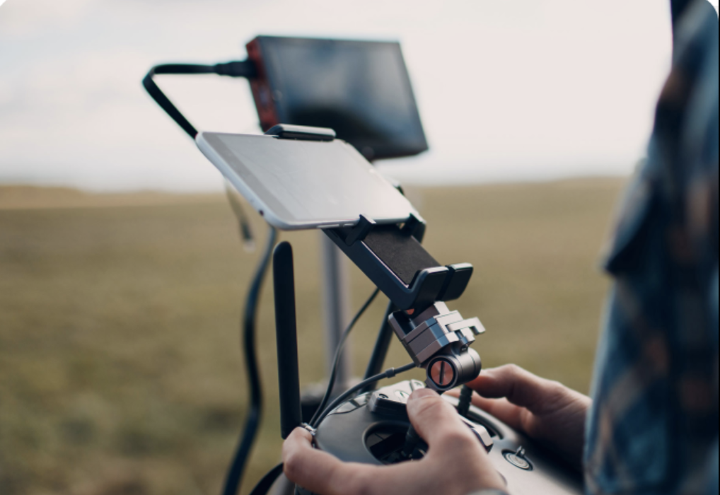 Person holding a remote controller with a smartphone mounted on it, outdoors with blurred grassy background.