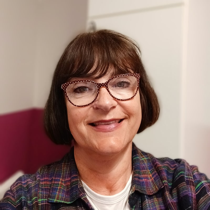 Attractive woman with short brown hair, smiling in red glasses and plaid shirt attire.