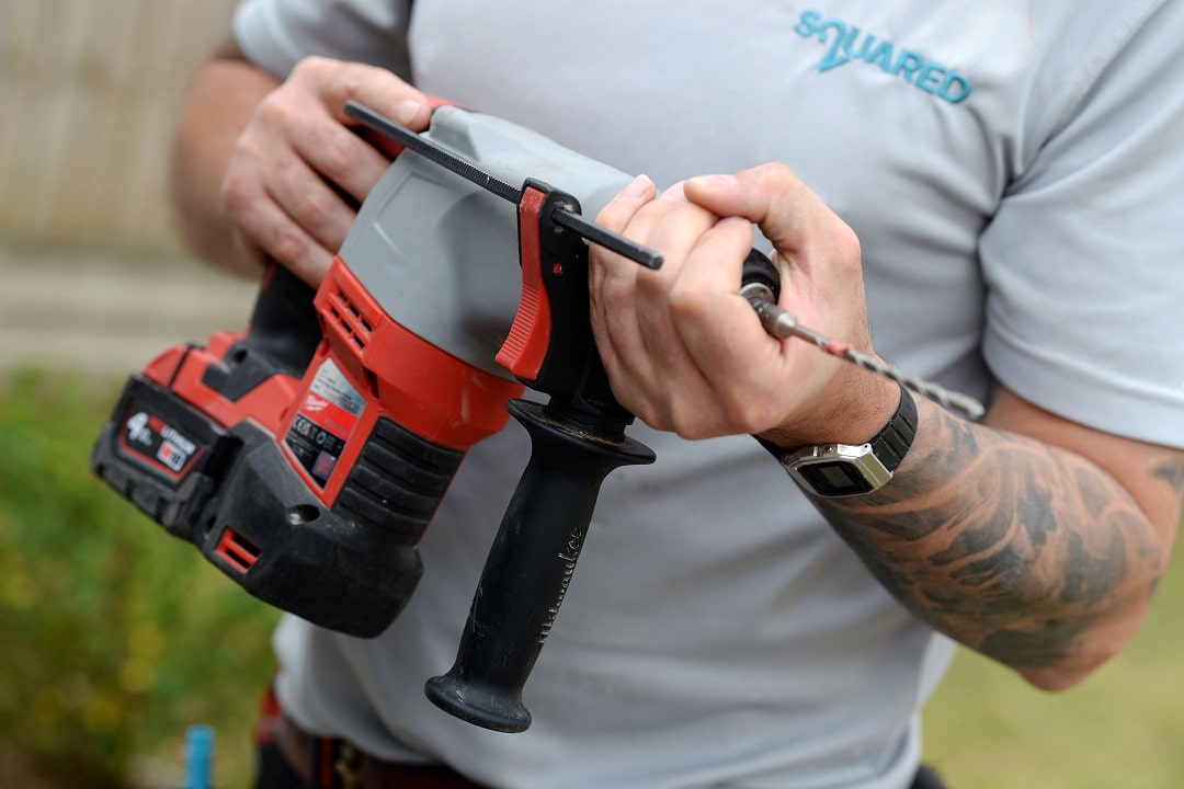 A handyman holds a red and black cordless drill outdoors with confidence steadily.