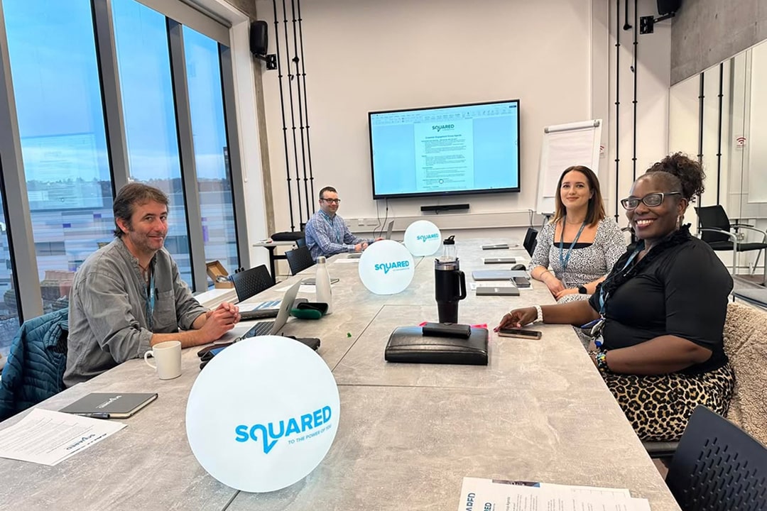 People collaborating around Squared branding and presentation screen at a corporate meeting workspace.