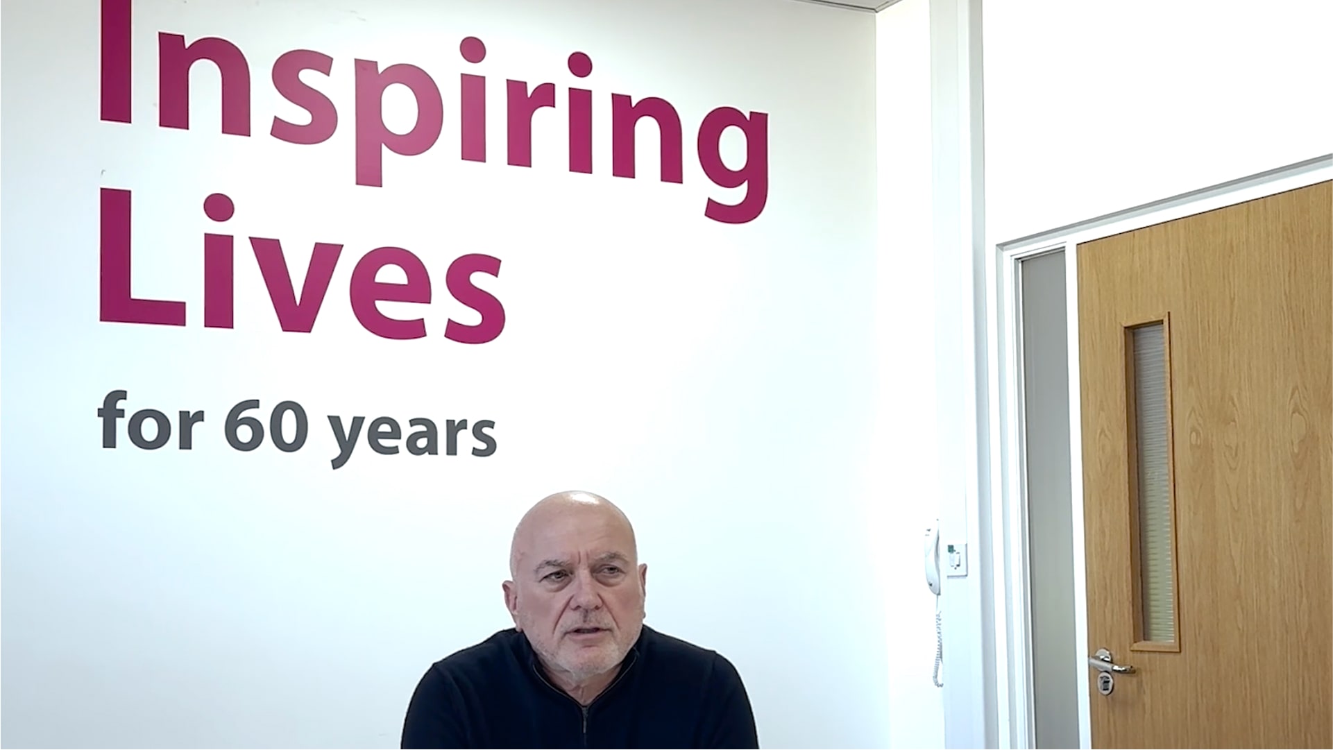 Man sitting in a reflective pose before a sign commemorating 60 years.
