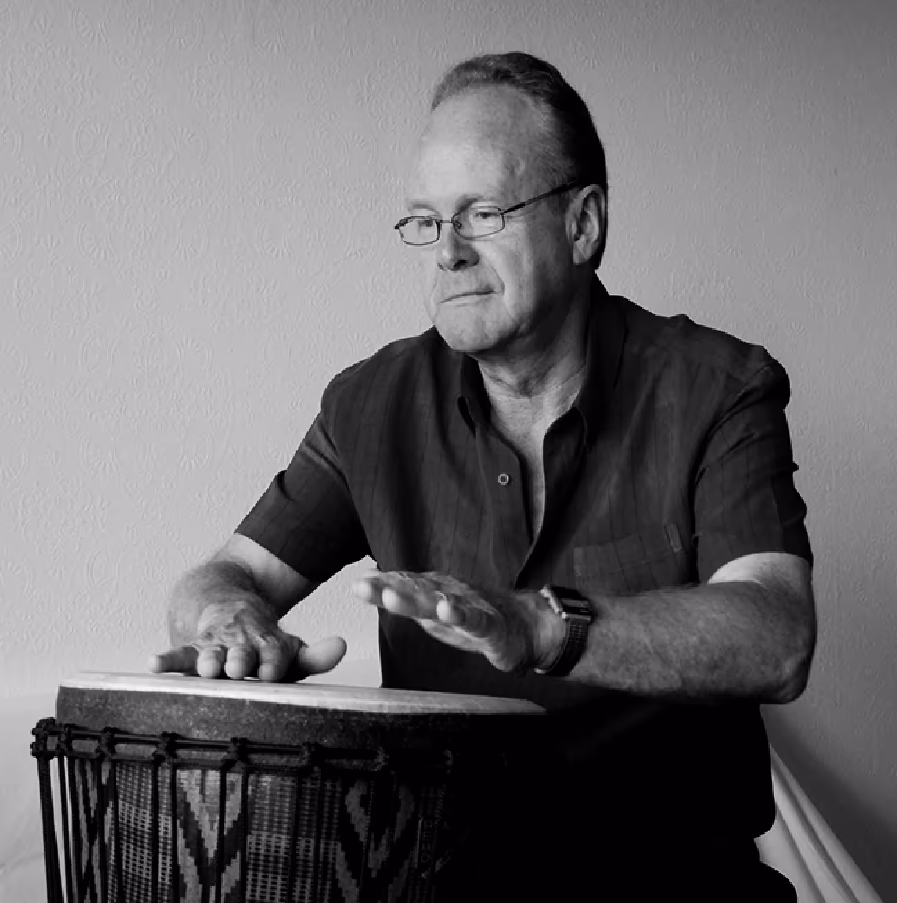 A man is playing a hand drum with a focused expression.