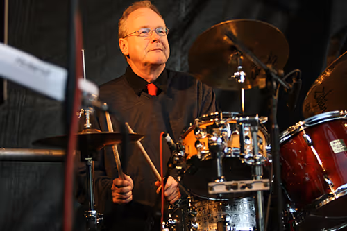A man is playing drums with drumsticks on a stage.