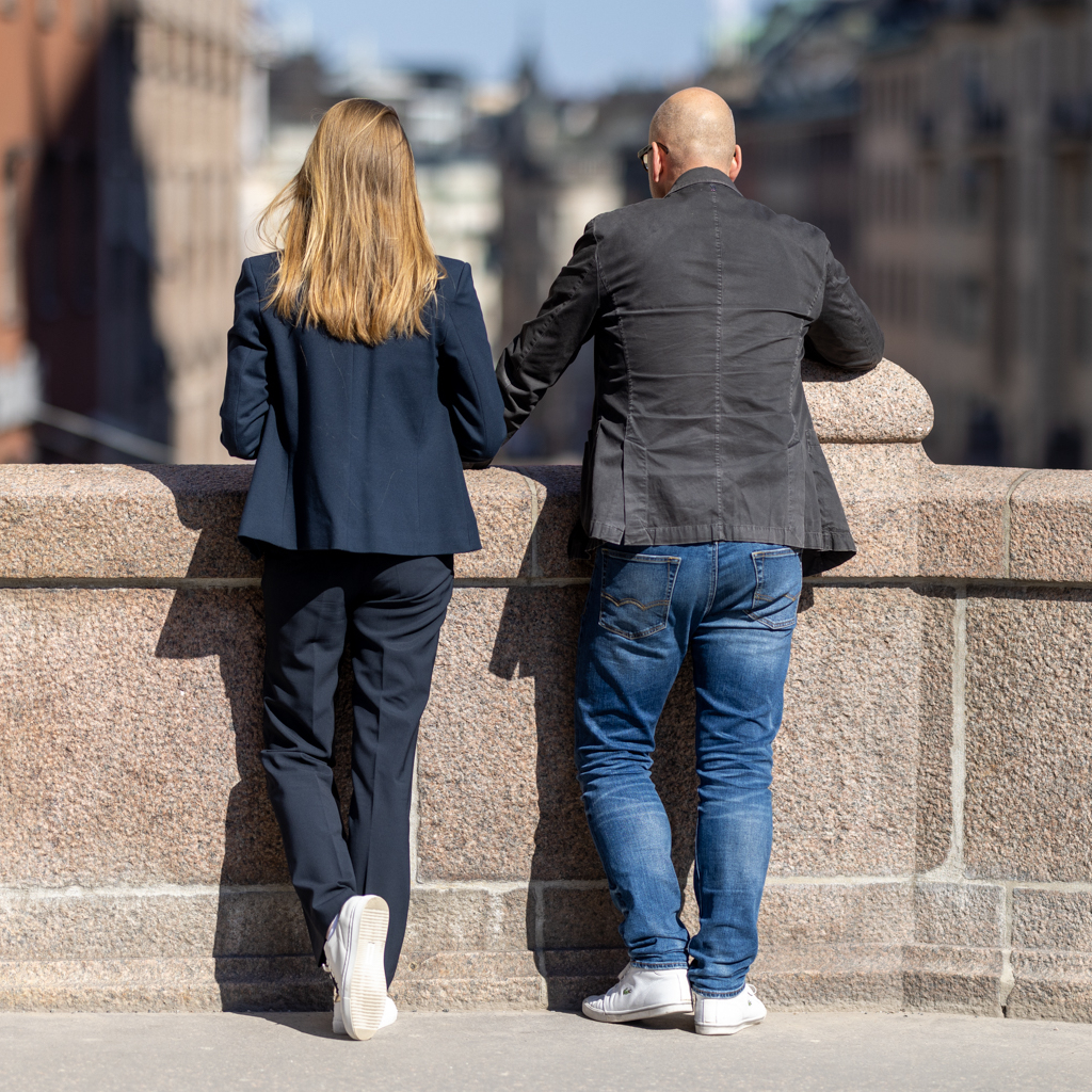 En man och en kvinna i businesskläder lutar sig mot en stenmur och tittar ut över en stad.