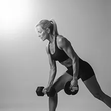 Fit woman performing a bent-over row exercise with dumbbells in a workout studio.