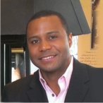 Portrait of a smiling man in a dark suit jacket and light pink shirt.