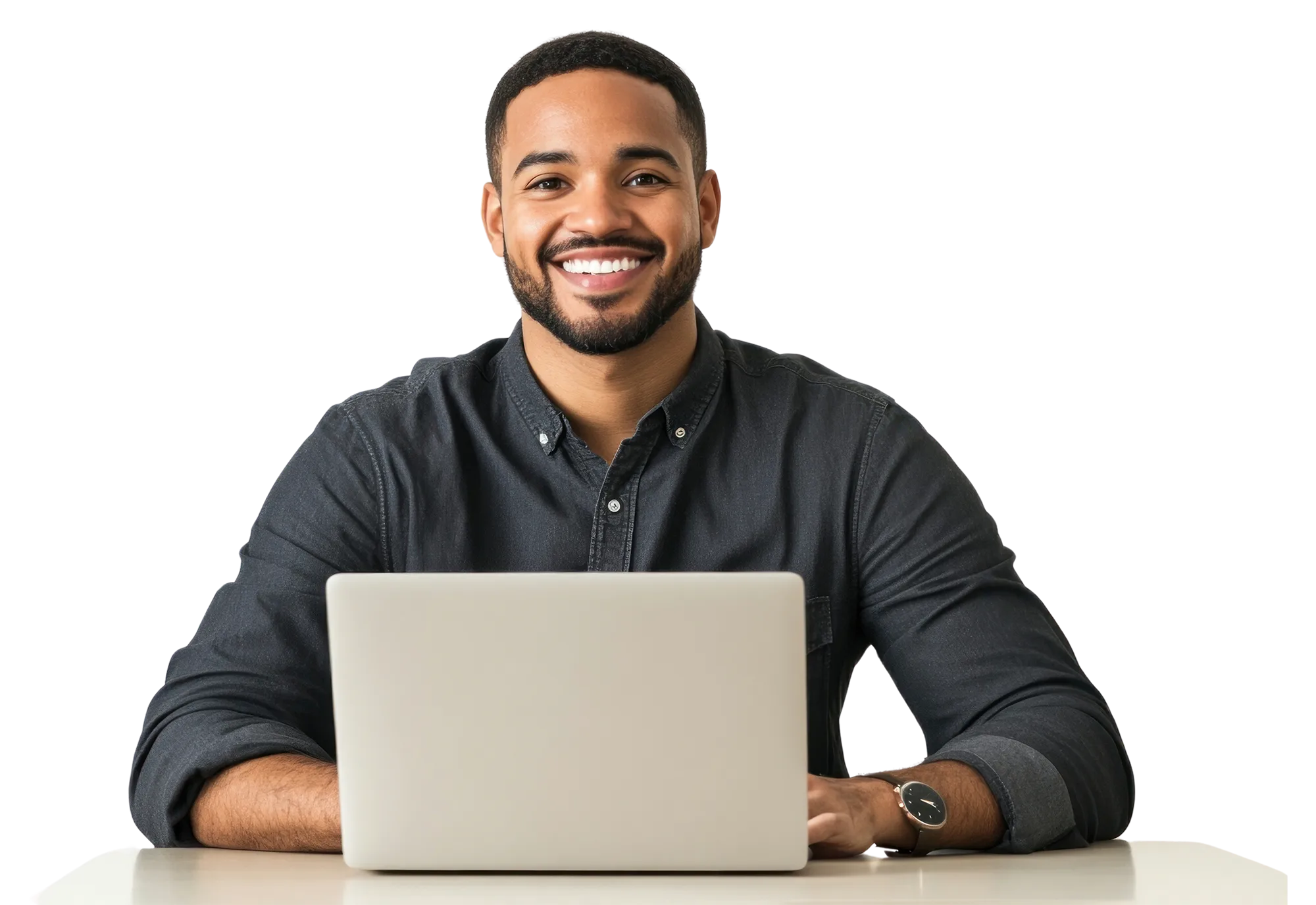 Smiling man with a beard wearing a dark button-up shirt sitting at a table with a laptop.