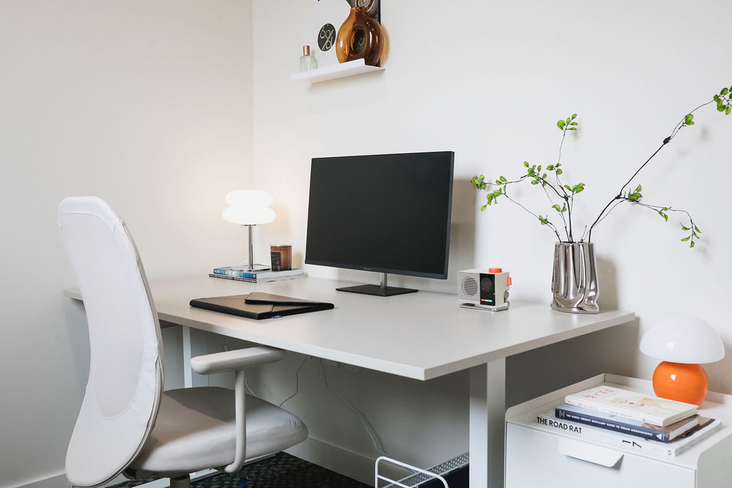 Private studio desk at Junto House with a monitor, task lamp, and shelf of books.