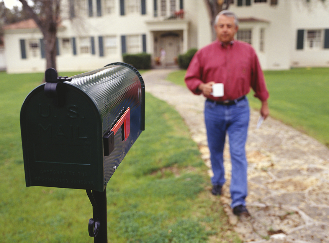 A man walking to his mailbox at the end of the driveway