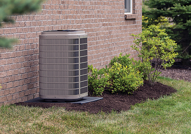 An air-source heat pump outside a home with green grass and trees