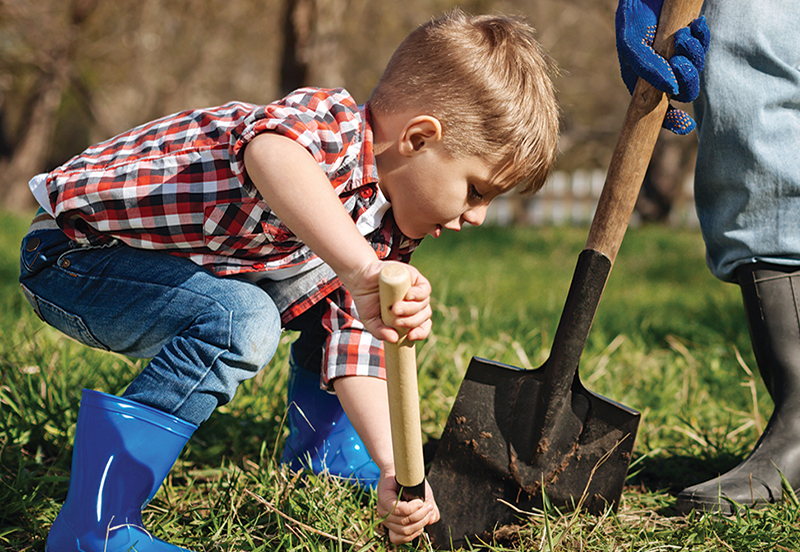 A young child helping someone dig a hole for a plant