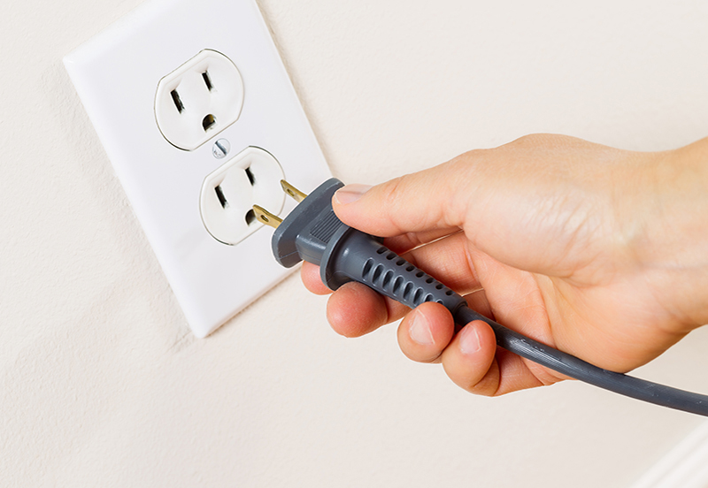 A hand plugging in a cord to an outlet