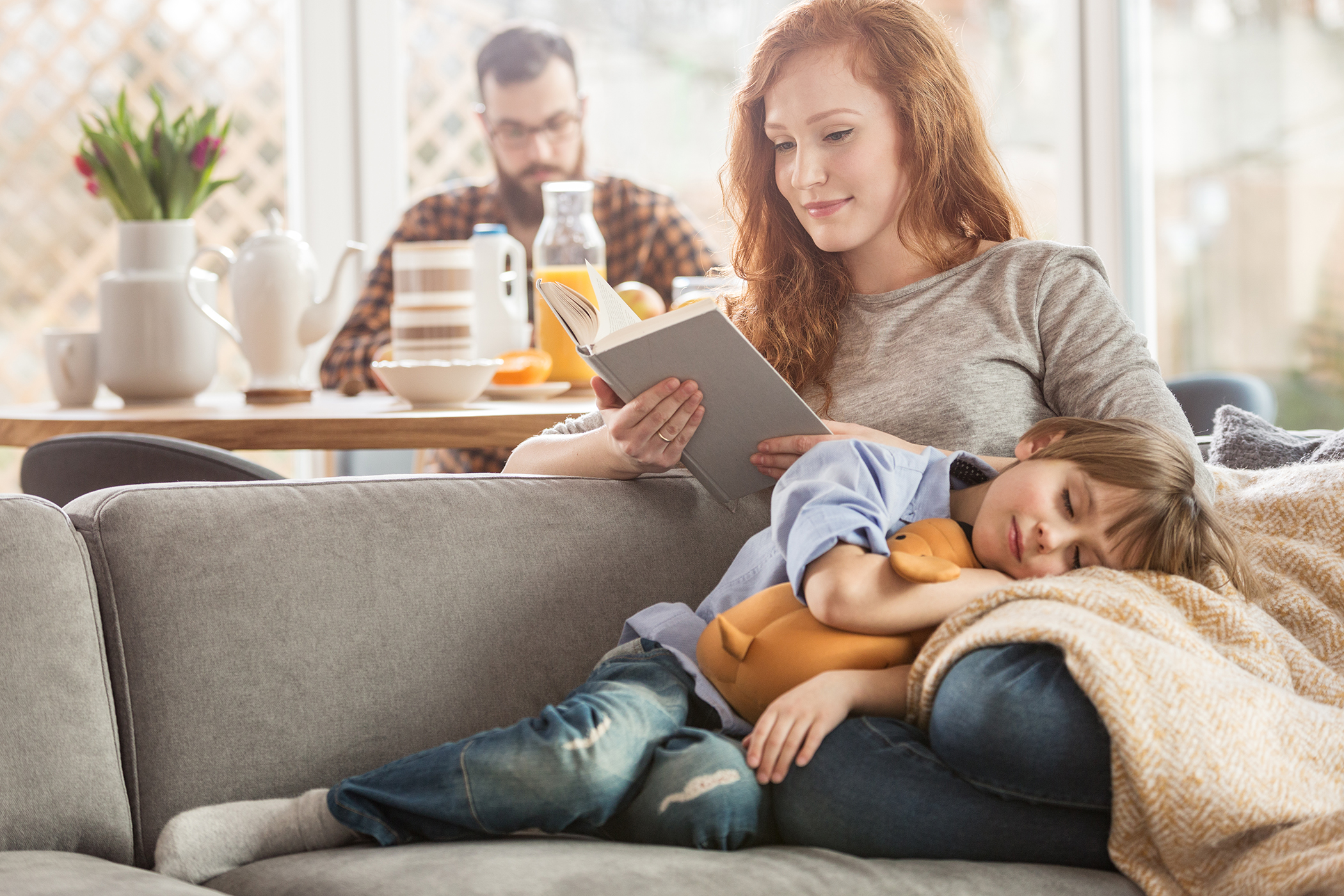 A mother reading on the couch with her son resting near her