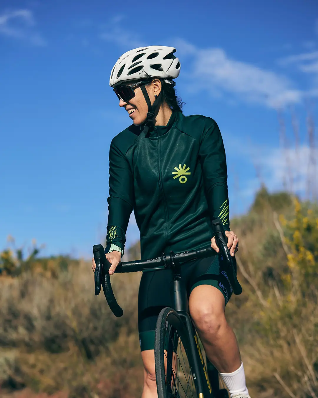 Female cyclist in green kit smiling on a road bike outdoors