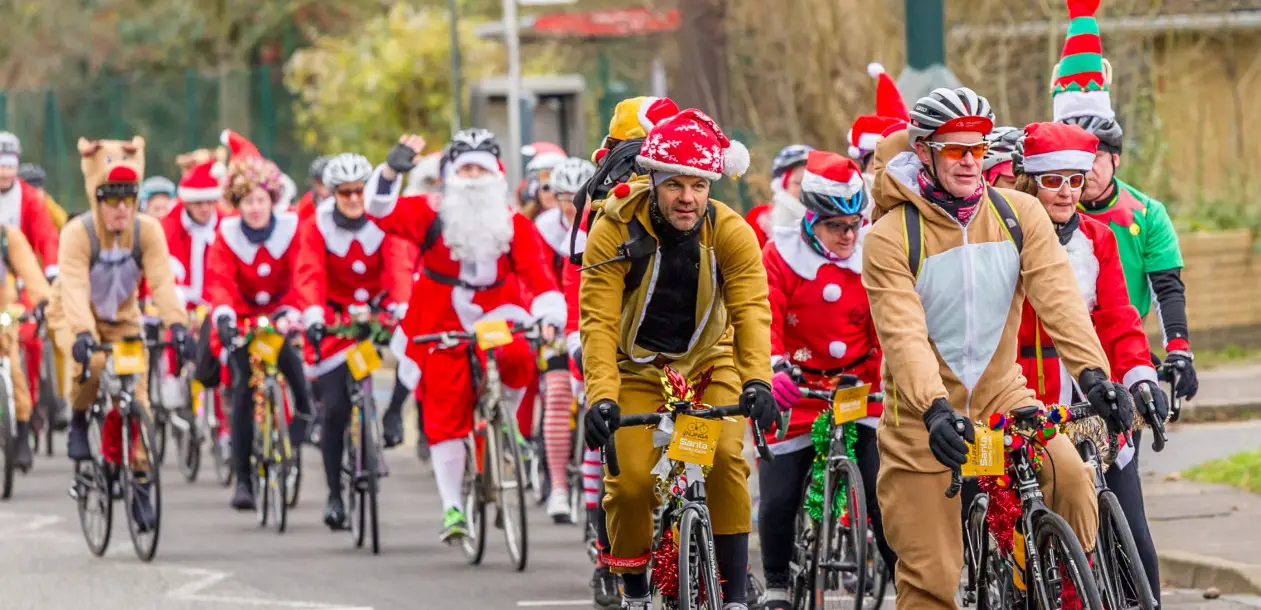 Festively dressed riders, including a reindeer costume, cycling in a group — sponsors welcome