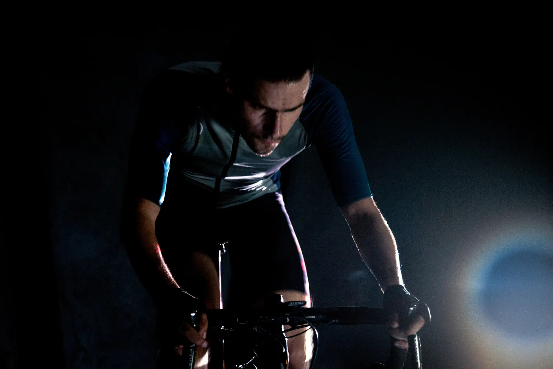 Cyclist riding indoors in low light, leaning over the bars during a hard effort.