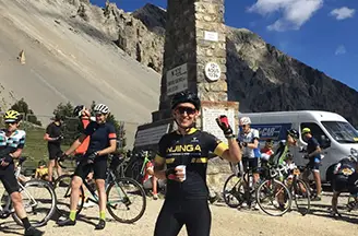 Njinga rider celebrates at the Col d’Izoard summit monument as cyclists regroup during a mountain challenge.