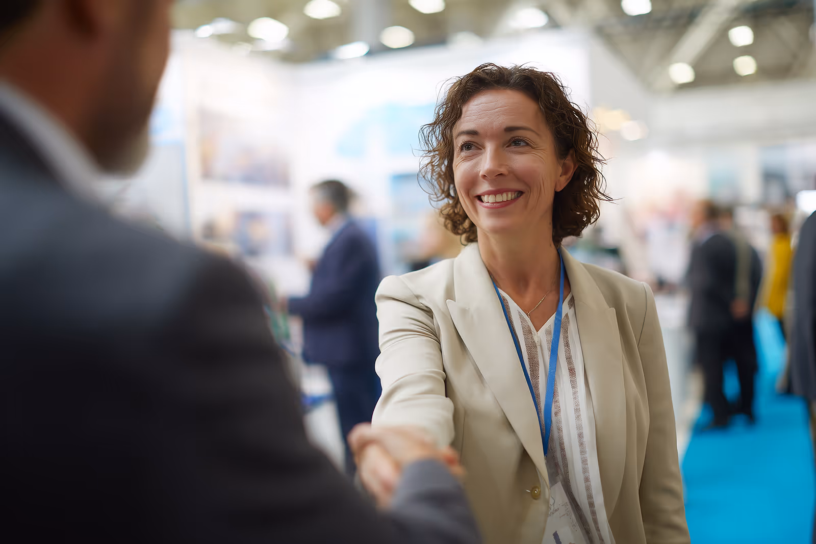 Businesswoman shaking hands with an attendee at a trade show, representing small and medium-sized enterprises preparing for export.