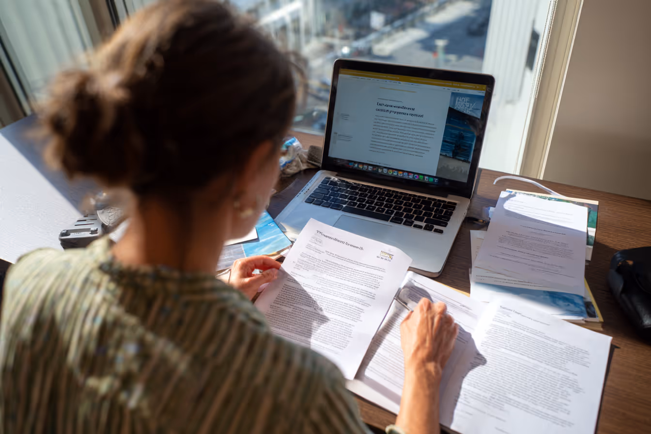 Person analyzing printed reports and charts beside an open laptop at a desk.
