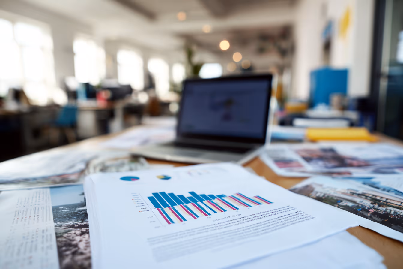 Open laptop on a desk surrounded by printed charts and documents showing industry data and analytics.
