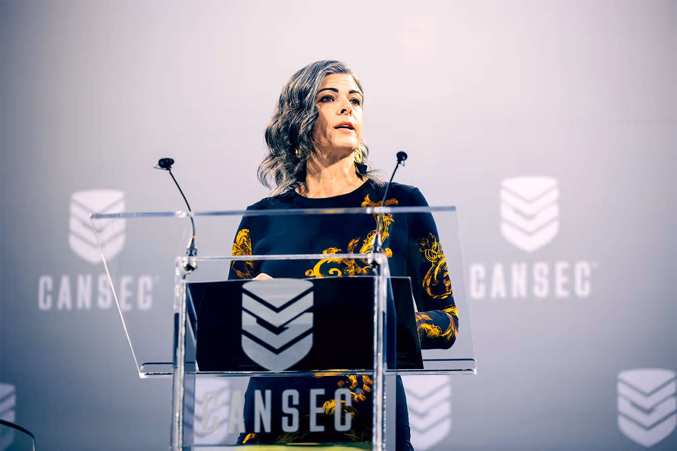Christyn Cianfarani prononce un discours sur le podium d'un événement CANSEC avec des microphones et une toile de fond de marque.