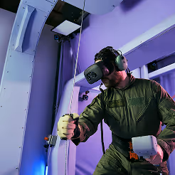 Military personnel wearing a VR headset and flight suit operating simulation equipment.