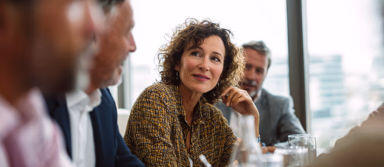 Diverse group of professionals seated around a meeting table, smiling and engaged in discussion.