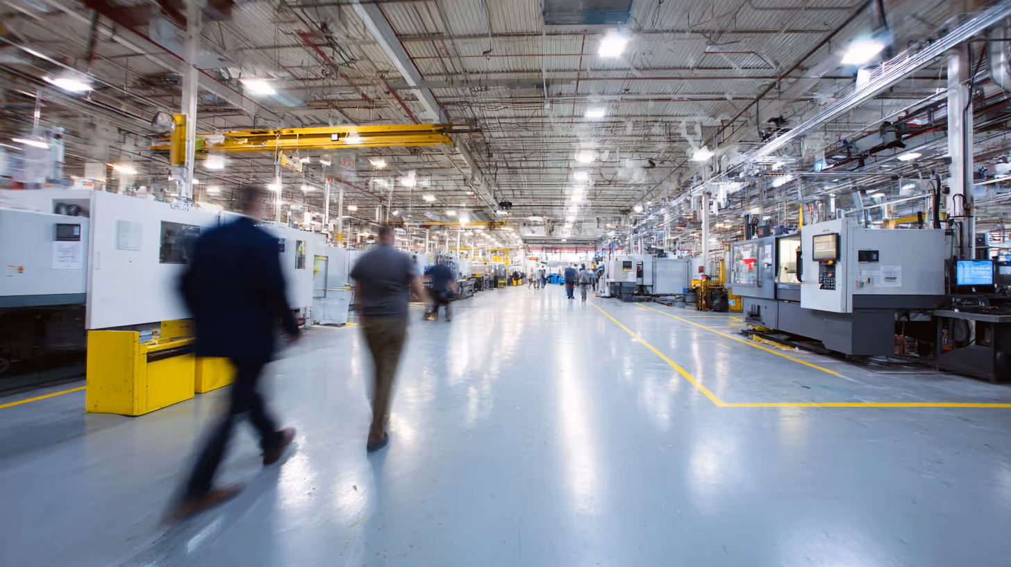 Workers walking through a bright industrial facility with machinery and overhead lighting.