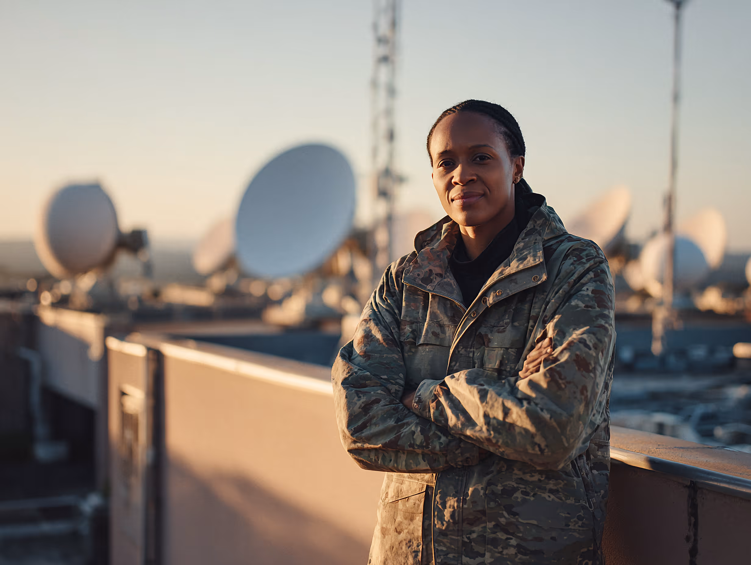 Communications engineer standing outdoors near satellite dishes at a defence communications facility.