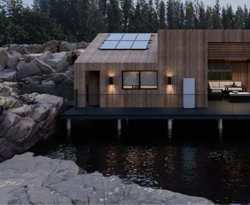 Modernt trähus vid vattnet med solpaneler på taket och hemmabatteri installerat på fasaden