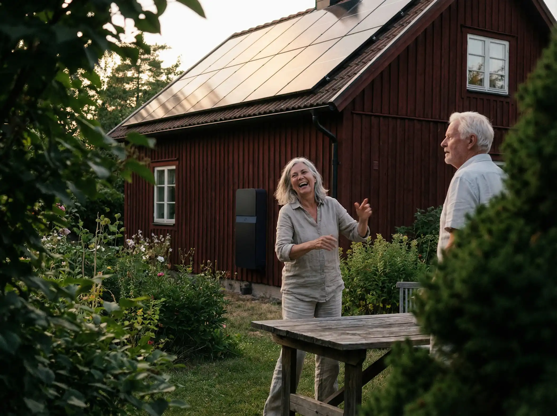 Två personer i trädgården utanför en röd villa med installerade solceller och hembatteri.