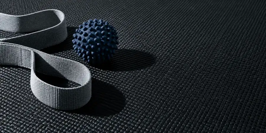 Sangle d'étirement et balle de massage posées sur un tapis de sol noir.
