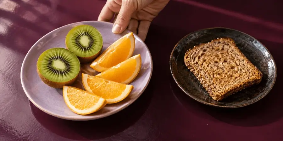 Une assiette de kiwis et de quartiers d'orange à côté d'une tartine de pain complet, des aliments qui accompagnent bien une prise de fer