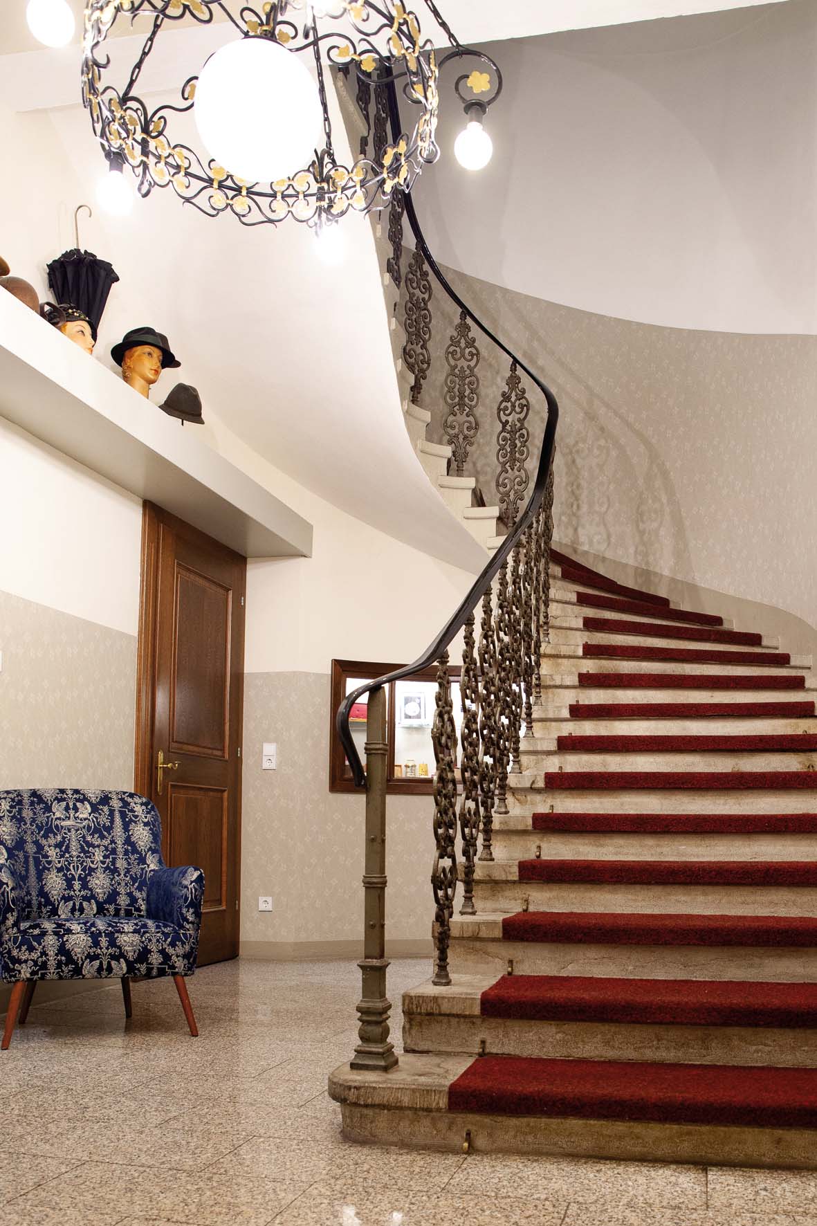 Elegante, geschwungene Treppe mit rotem Teppich und verziertem Geländer in einem stilvoll eingerichteten Raum mit blauer gemusterter Couch.