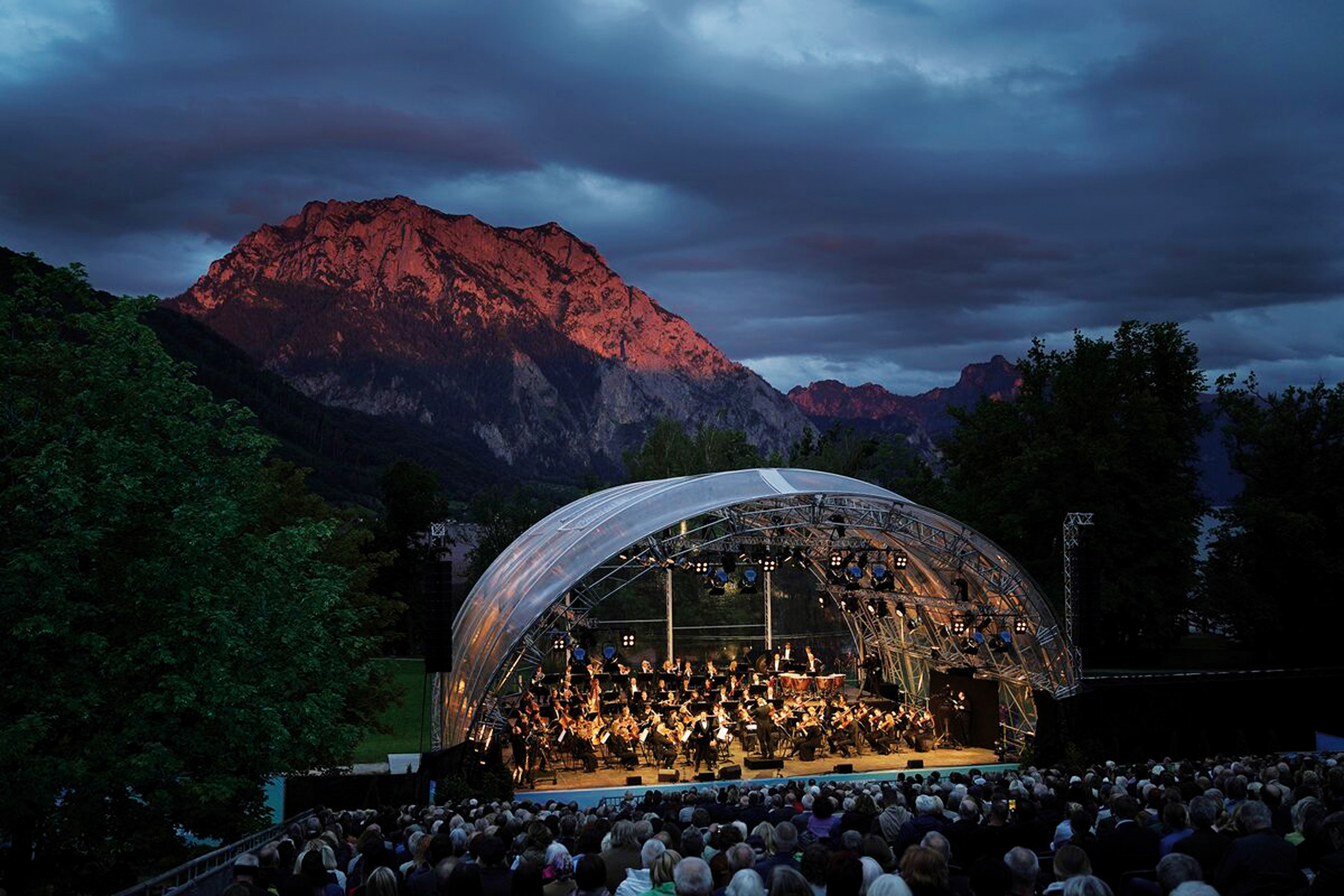Open-Air-Orchesterkonzert bei Dämmerung mit beleuchteter Bühne vor Bergen im Salzburger Land.