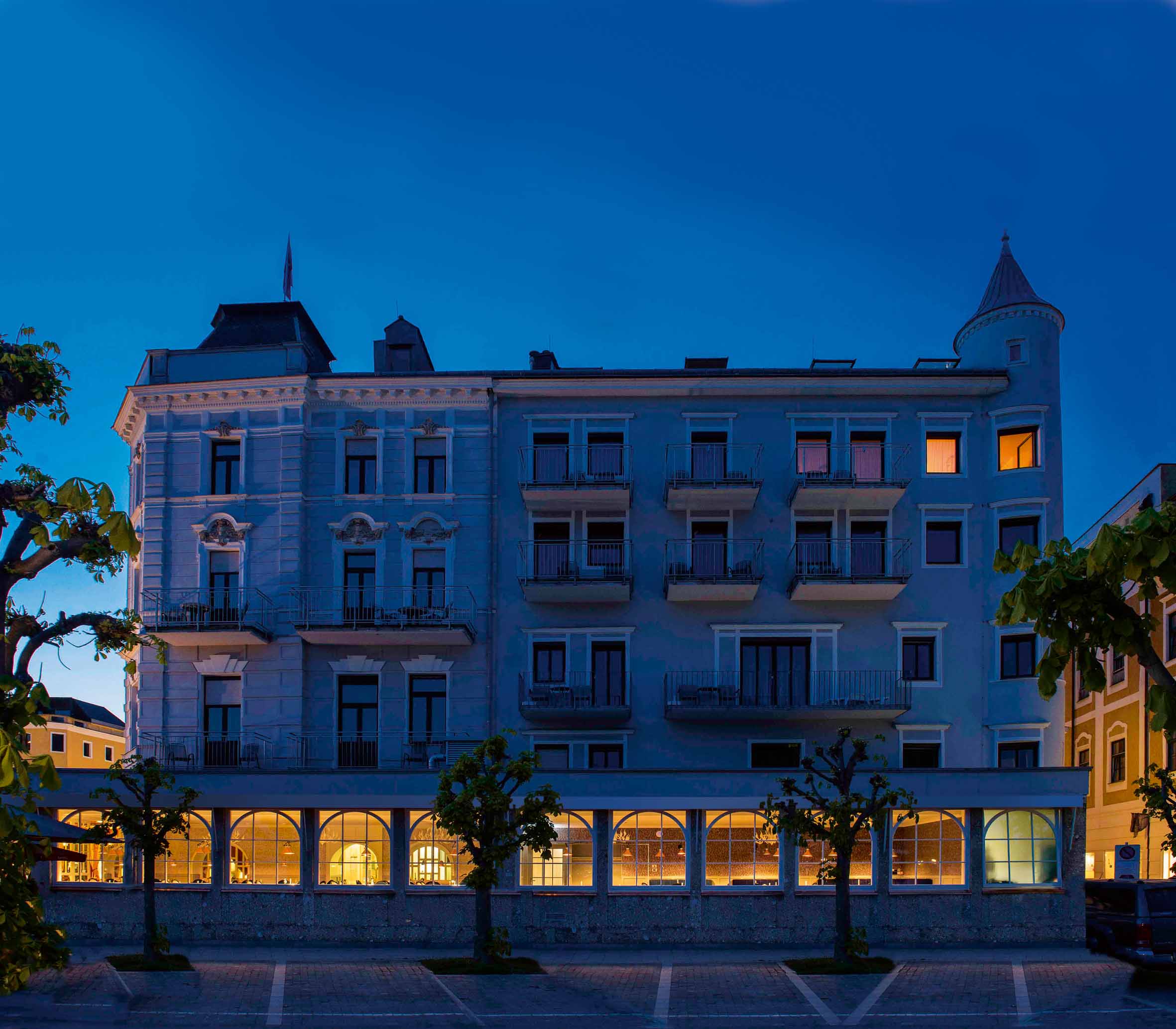 Beleuchtetes historisches Hotelgebäude mit Balkonen und Turm bei Nacht.